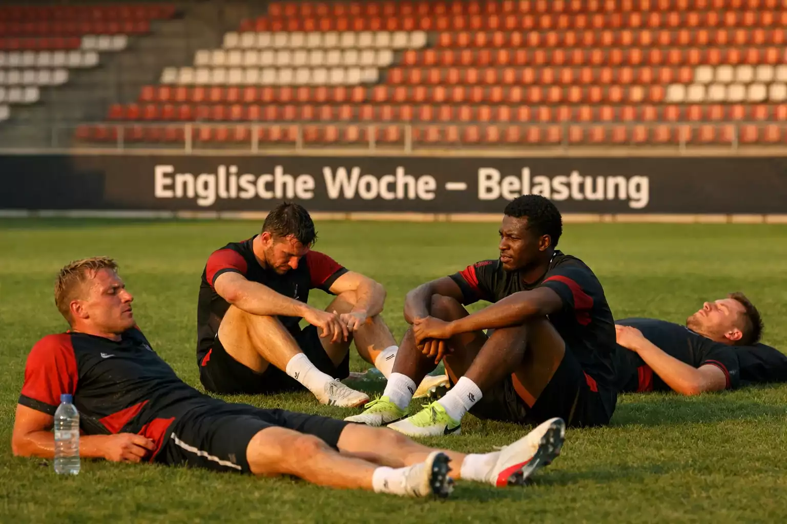Erschöpfte Fußballspieler ruhen sich nach dem Training auf dem Rasen eines Bundesliga-Stadions aus